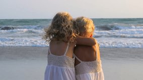View from back little twin girls hugging and admiring ocean at sunset. Children look at big waves ocean and strong wind blows white curly hair. Children friendship and carefreeness by powerful ocean. - Powered by Shutterstock - Get 15% off with code: PIKWIZARD15