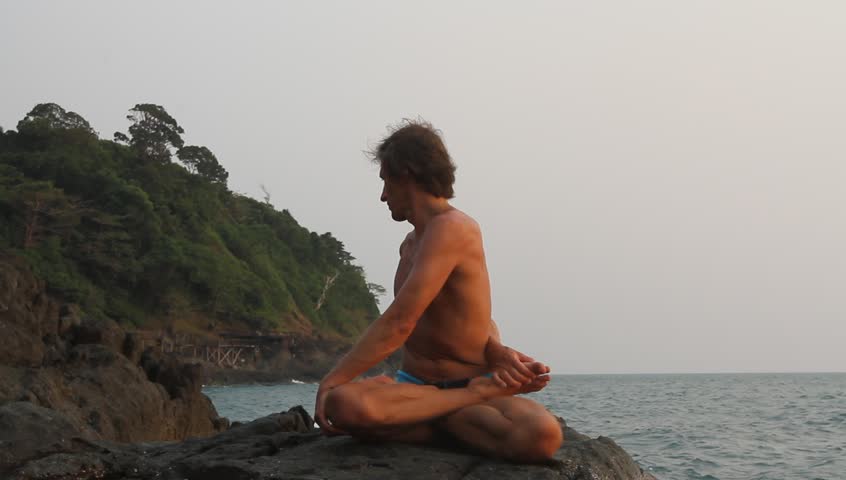 Man doing yoga exercise on the deserted wild stone sea beach