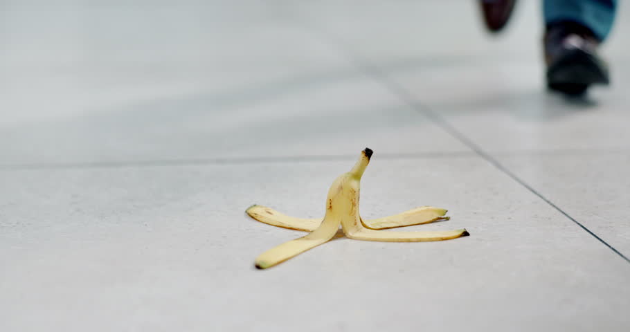 Office, fall and person with banana on floor for accident, medical emergency and injury from walking. Corporate, workplace safety and feet of worker slip on fruit for danger, law suit and risk