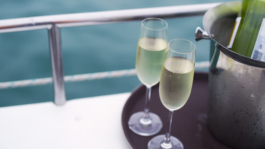 Champagne bottle in ice bucket with champagne glass on the tray for serving to passenger tourist on luxury catamaran boat yacht sailing in the ocean at sunset on summer holiday travel vacation trip.