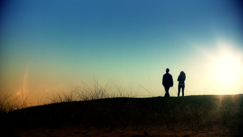 Couple walking on green meadow at sunset