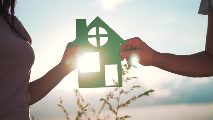 Family mortgage concept. Family holds paper house with their hands at sunset. Family house on loan. Paper house is symbol of family happiness.Housing and mortgage crisis.Dream concept of buying house