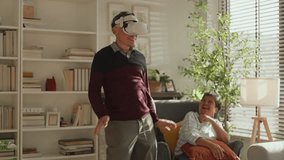 Asian mature retired Senior man wearing a vr headset adance and body humor moving around while looking around in virtual world in living room with hie wife cheering laugh healthy insurance lifestyle - Powered by Shutterstock - Get 15% off with code: PIKWIZARD15