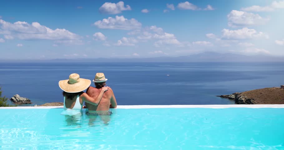 A couple hugging at the edge of an infinity pool and enjoying the view to the blue, mediterranean sea during summer vacation time