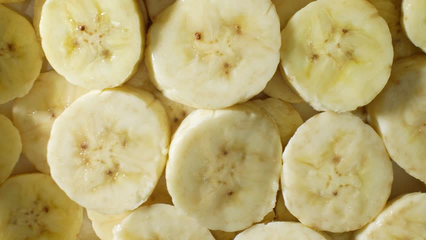 A mesmerizing close-up captures the creamy allure of sliced bananas. Each uniform piece unveils a soft, buttery texture, adorned with delicate brown speckles amidst its gentle yellow hue.
