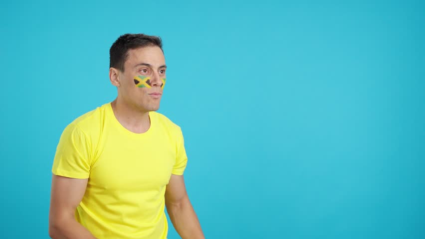 Man cheering for Jamaica waving a national flag looking away