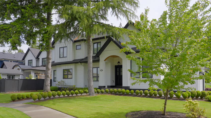 Establishing shot of two story stucco luxury house with garage door, big tree and nice spring blossom landscape in Vancouver, Canada, North America. Day time on June 2024. ProRes 422 HQ.