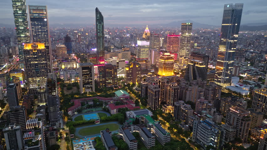 Aerial hyperlapse at dusk above Downtown Taipei, vibrant capital of Taiwan, with 101 Tower standing out amid skyscrapers in XinYi Commercial District and city lights dazzling under moody twilight sky