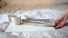 Morning Routine With Coffee And News. Hand reaching for a newspaper next to a cup of coffee on a white bed, representing a relaxed and serene morning routine. - Powered by Shutterstock - Get 15% off with code: PIKWIZARD15