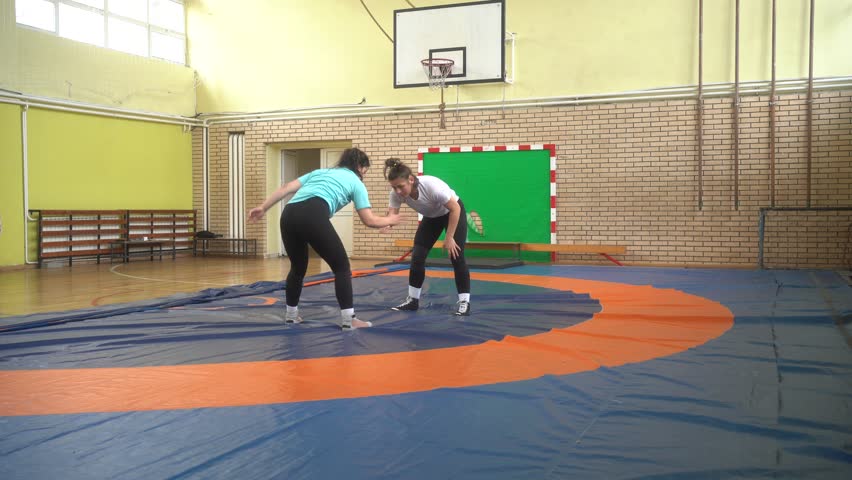 Two strong female wrestlers one-arm shoulder throw. Shoulder Flip Over. Female freestyle wrestling training in the gym. Medium shot