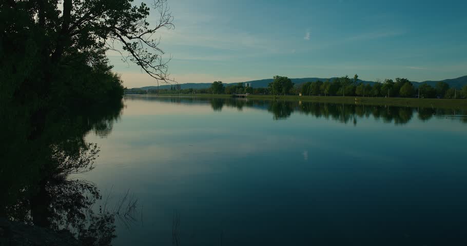 Serene lake with tree reflections and mountains in the background at sunset in Jarun Lake, Zagreb Croatia