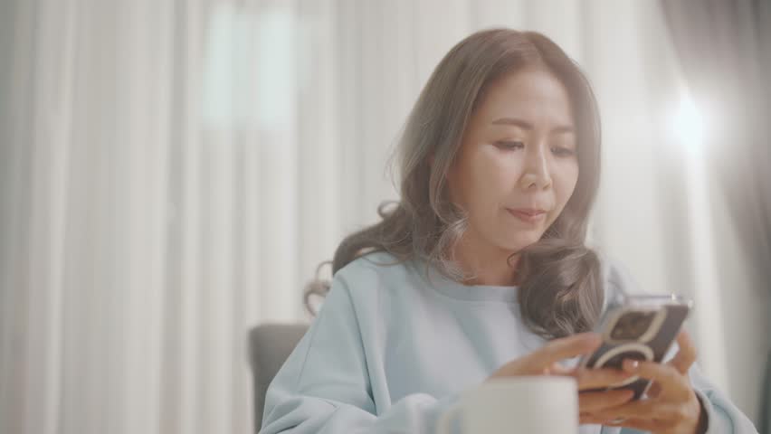 Women are playing with their mobile phones on the sofa and on the dining table and drinking coffee at the same time.
