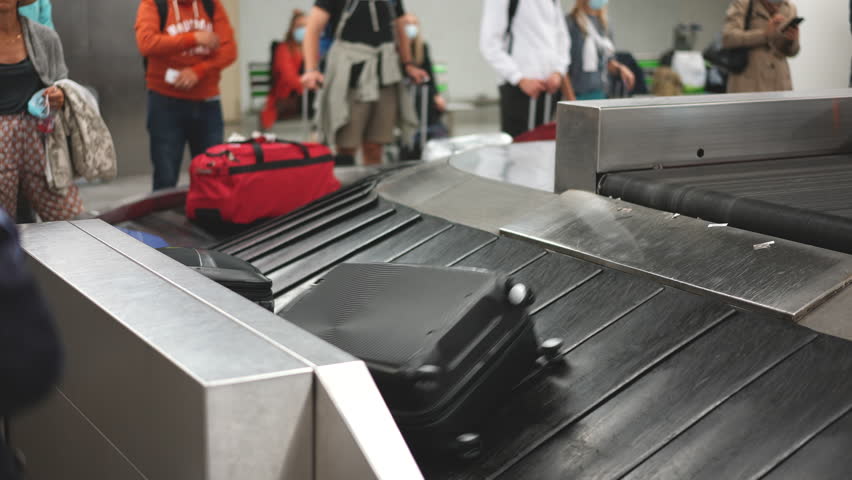 Many suitcases move conveyor belt. Lots of people wait baggage after arrival. Airport bags carousel. Hand luggage check in area. Train station travel. Tourist personal baggages. Busy queue. Fly trip.