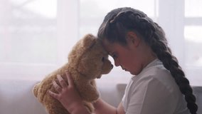 depressed girl child sitting by window with her favorite toy teddy bear upset. problem of domestic violence in the family concept. depressed girl is sunlight sad and bored at window with bear - Powered by Shutterstock - Get 15% off with code: PIKWIZARD15