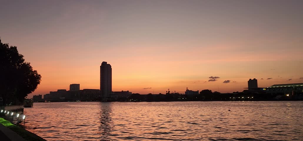 Rama VIII Bridge is asymmetrical single-mast bridge on the13th Chao Phraya river in Bangkok. This clip is surrounding atmosphere in the evening. Sky is orange, reflecting Chao Phraya River as sunset.
