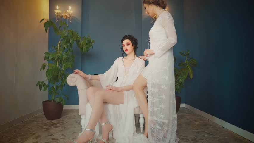 Two Fantasy women Sexy girl maid beauty strong face power queen woman sitting on throne chair in luxury blue classic room. Long vintage silk white dress fairy style noble lady fashion model posing 4k.