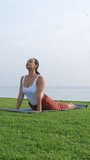 Vertical video. Morning yoga asana of young woman by the seashore, slow motion. Female working out on mat outdoors