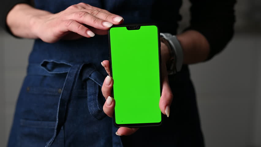 Girl In Apron Holding A Smartphone With A Green Chromakey Screen - Powered by Shutterstock - Get 15% off with code: PIKWIZARD15
