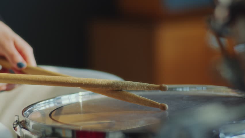 Hands of unrecognizable female drummer hitting drums with sticks while playing music on a drum kit. Close-up shot