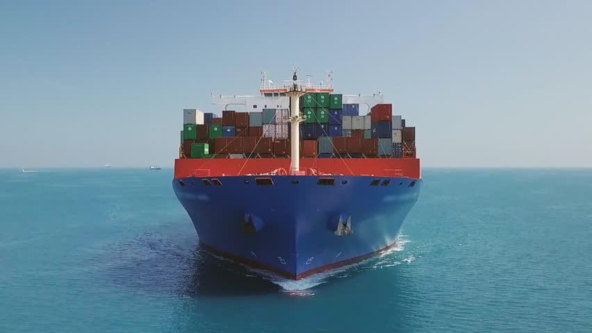 Slow Mo. Flying low over a container ship from nose side to center. A huge cargo ship, 300x48 meters long and wide, sails in open Sea
