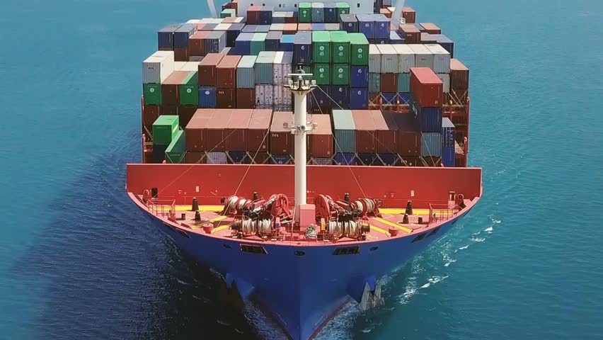 Slow Mo. Flying low over a container ship from nose side to center. A huge cargo ship, 300x48 meters long and wide, sails in open Sea
