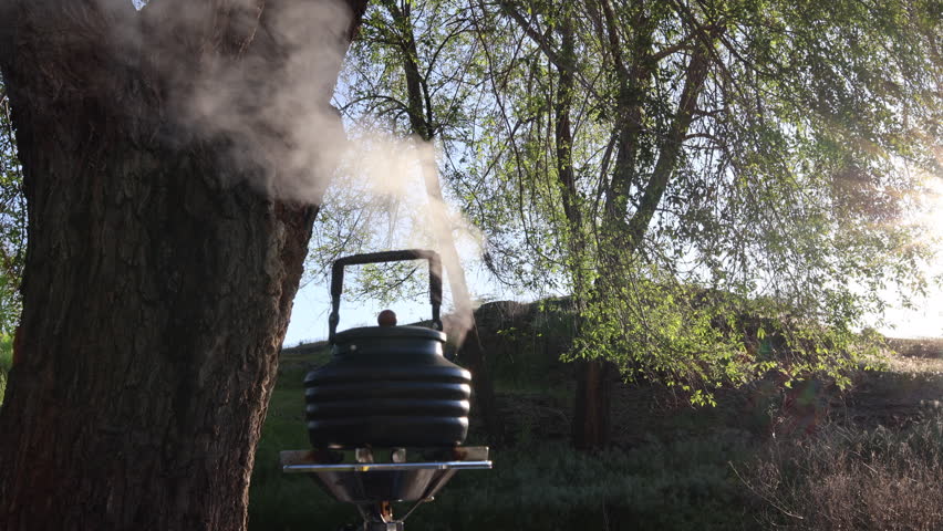 Teapot kettle steaming in the cool spring morning water boiling within heated by a propane stove at camp