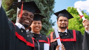 Happy multiracial group of students in graduation dresses and hats taking selfie together - Powered by Shutterstock - Get 15% off with code: PIKWIZARD15