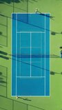 Vertical Screen: Observe an exhilarating aerial perspective of a tennis match on a colorful court in the sunlight, players displaying energy and strategic prowess in their dynamic movements