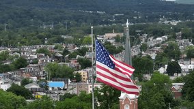 American flag waving over neighborhood and church in city of USA. Sunny day with green trees on hill in town. Aerial close up orbit. - Powered by Shutterstock - Get 15% off with code: PIKWIZARD15