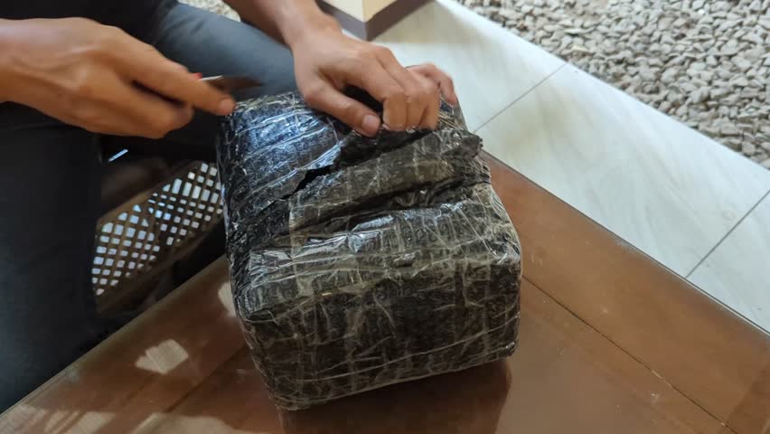 A male hand using sharp cutter knife slashing black box packing bubble wrap, in the wood table, unboxing of the e-commerce internet order box,4K.