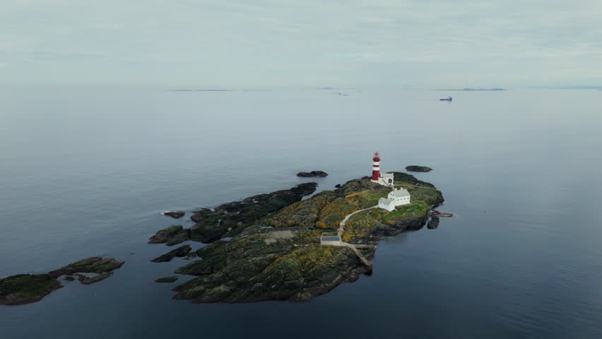 Aerial establishing shot of a red and white striped lighthouse in Norway