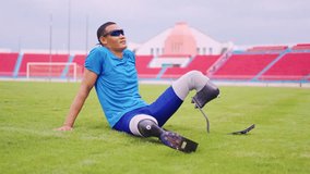 Asian para-athlete with prosthetic blades stretching leg in stadium. Attractive amputee sportsman runner sitting on floor, taking a break after practicing workout for Paralympics running competition - Powered by Shutterstock - Get 15% off with code: PIKWIZARD15