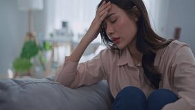 Asian upset depressed woman sitting alone on sofa in living room at home. Attractive unhappy young femlae feeling sad, lonely and upset with life problem then crying with tears in quiet room in house. - Powered by Shutterstock - Get 15% off with code: PIKWIZARD15