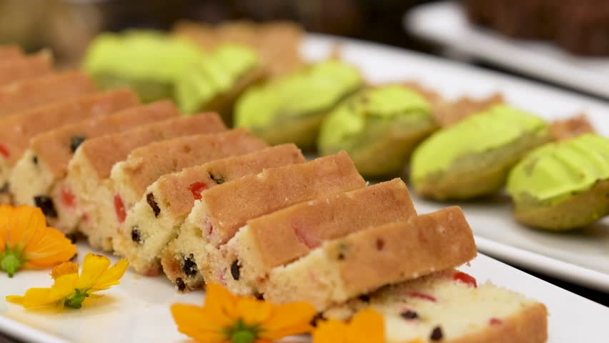 A beautifully decorated catering banquet table with a variety of cakes. Buffet food is set up for corporate event.
