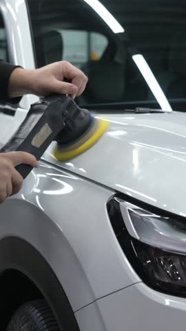 A mechanic polishes the surface of the body of a white car. Body repair. Vertical video.