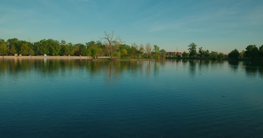 Wide view of a calm lake with tree reflections and a clear sky at Jarun Lake, Zagreb Croatia