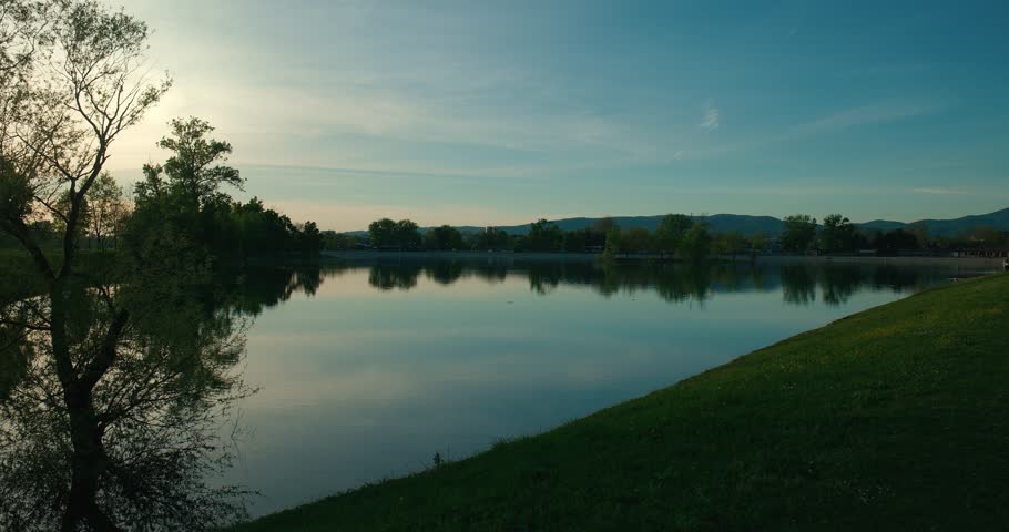 Serene lake with tree reflections and mountains in the background at sunset in Jarun Lake, Zagreb Croatia