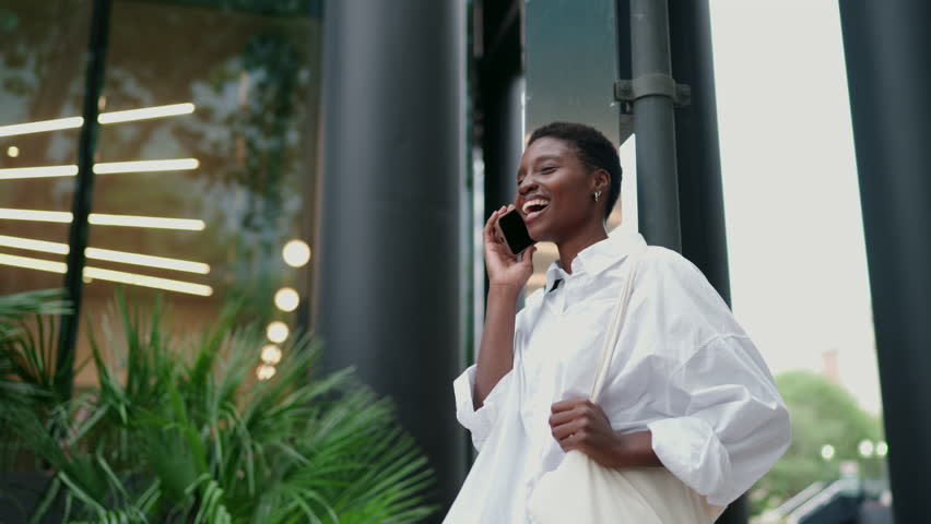 Happy African American female using modern communication, feeling joy of staying connected with loved ones or conducting business on the go. Cheerful black young woman have mobile phone call outdoors