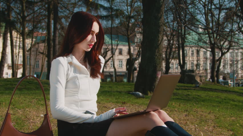 Young Atractive Student Doing Homework In Central Park. 4k video. 
Breautiful Lady Working On Laptop while sitting on grass at city ​​grove and enjoying sunbeams. 