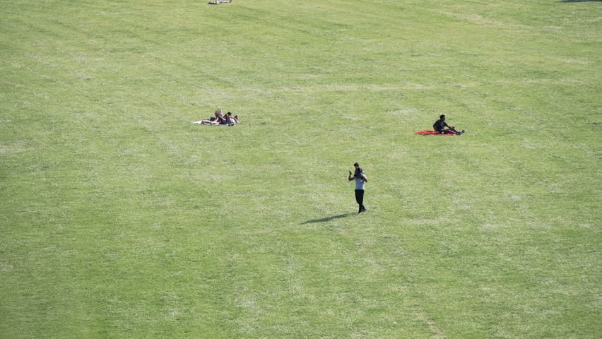 Aerial view of serene Rhinepark scene in Cologne, Germany with perople relaxing. Father takes child piggyback playing in park, slow motion. Individuals walking on a bright sunny day