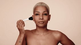 A portrait of a confident, bare-shouldered woman applying makeup with a cosmetic brush against a neutral backdrop. - Powered by Shutterstock - Get 15% off with code: PIKWIZARD15