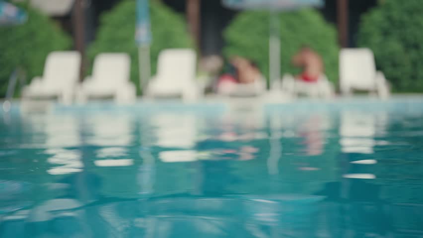 Serene pool establishing view with blurred people relaxing on vacation and clear calm water surface moving in slow moiton