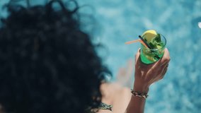 A woman relaxes by a sparkling pool, holding a mojito with a slice of lemon. The focus is on summer relaxation and enjoyment in a tropical setting. - Powered by Shutterstock - Get 15% off with code: PIKWIZARD15