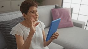 Elderly hispanic woman with short hair making a video call on a blue tablet in her cozy living room. - Powered by Shutterstock - Get 15% off with code: PIKWIZARD15