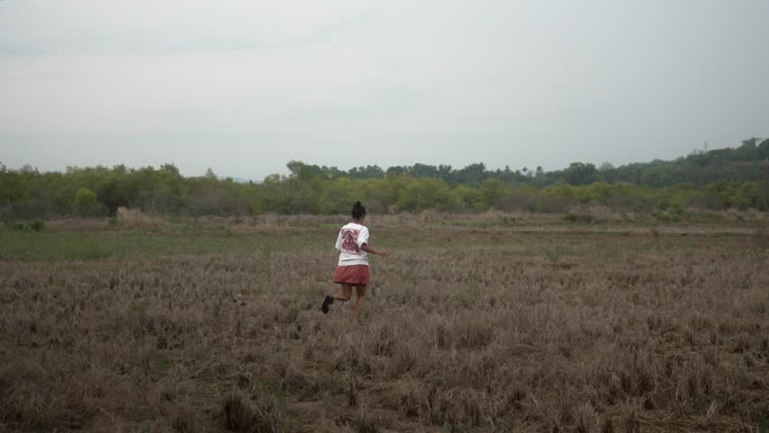 Person running across an open field with greenery and hills in the background