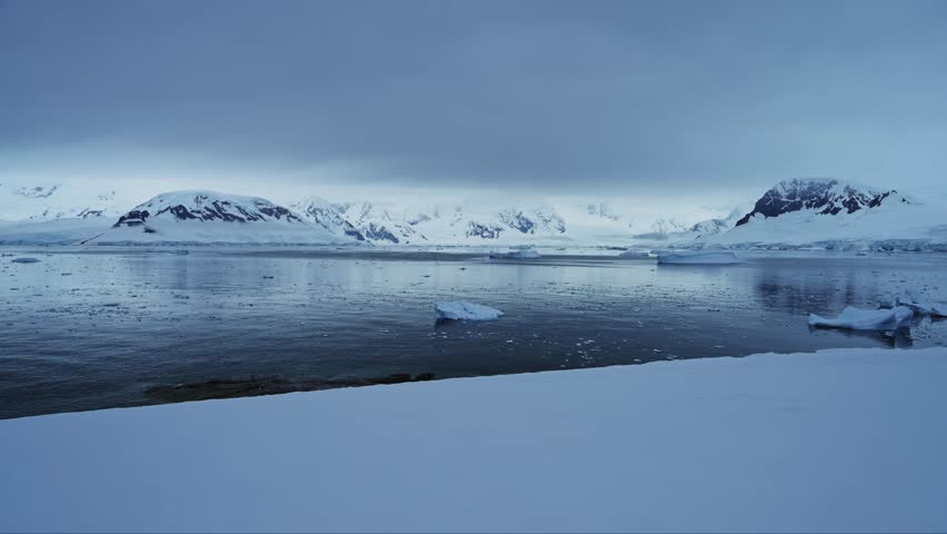 Antarctica Mainland Coastal Scenery on Coast, Winter Landscape with Snow Ocean and Mountains, Icebergs in Sea in Beautiful Dramatic Dark Moody Blue Seascape on Antarctic Peninsula