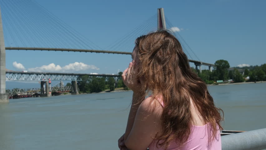 a young girl relaxes on the embankment overlooking the bridge, river, warm sunny summer day. Skytrain Bridge in New Westminster and Surrey, Greater Vancouver, British Columbia, Canada.