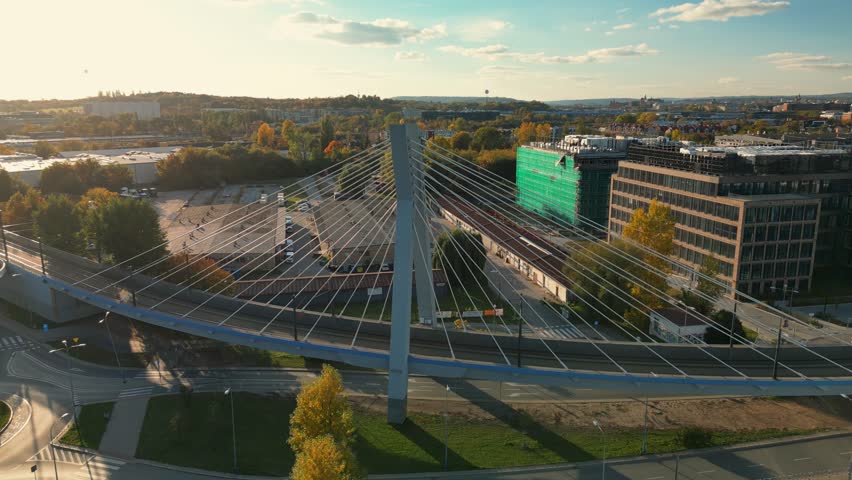 Scenic panoramic aerial cityscape with suspension bridge, moving tram in Krakow, Poland. Perspective above view of high modern bridge structure, street buildings.
