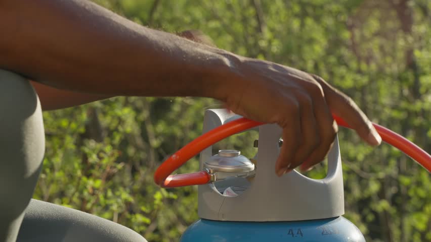 African American man setting down gas bottle and hooking up hose for grill