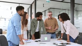 Diverse team huddles around table, and looks at a laptop screen in a bright office, closely reviewing documents and digital content together, showcasing a moment of collective focus and determination - Powered by Shutterstock - Get 15% off with code: PIKWIZARD15